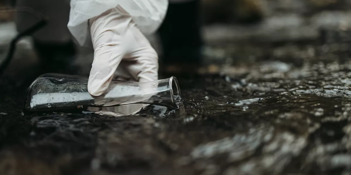 A person sampling fresh water using a test beaker in open environment. Evaluation exposure assessments and toxicity evaluations.