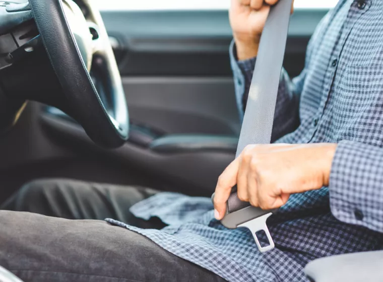 A shot of a person in the behind the steering wheel of a car buckling their seatbelt