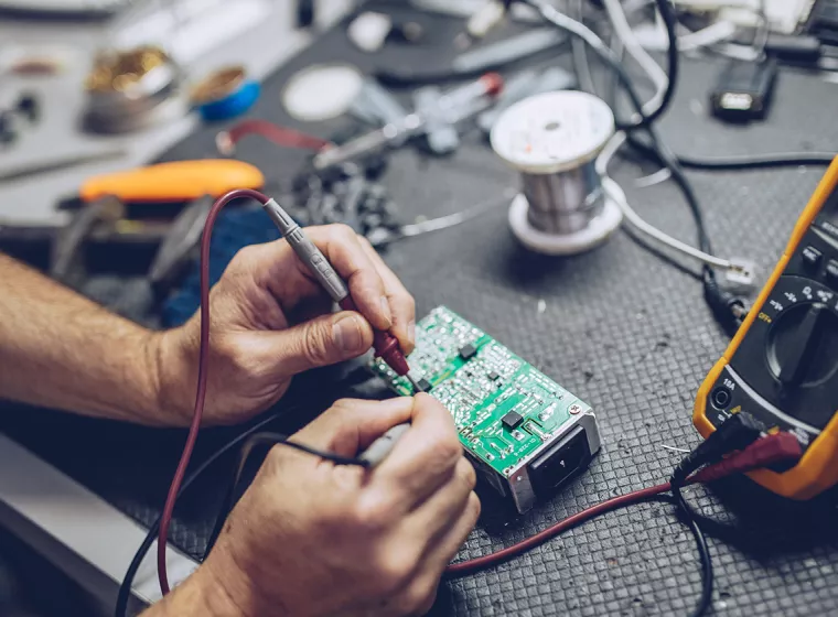 Worker testing electrical computer components using digital multimeter. Exponent conducts technical forensics investigations.