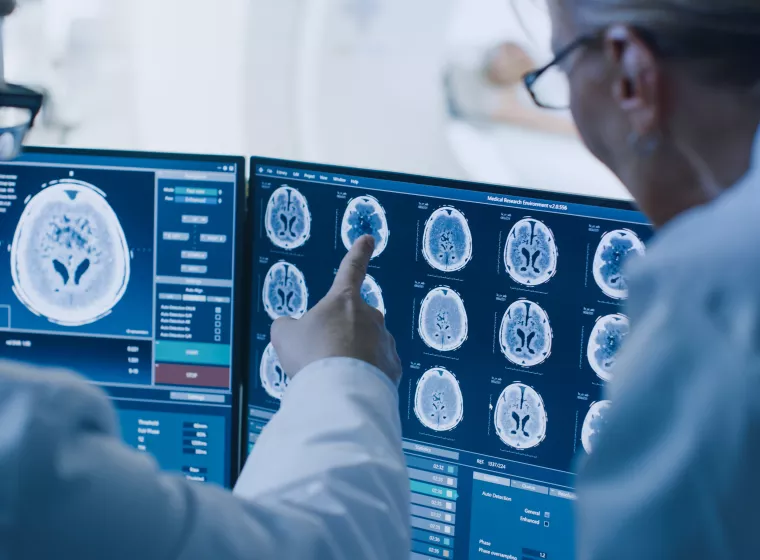 In Control Room Doctor and Radiologist Discuss Diagnosis while Watching Procedure and Monitors Showing Brain Scans Results, In the Background Patient Undergoes MRI or CT Scan Procedure