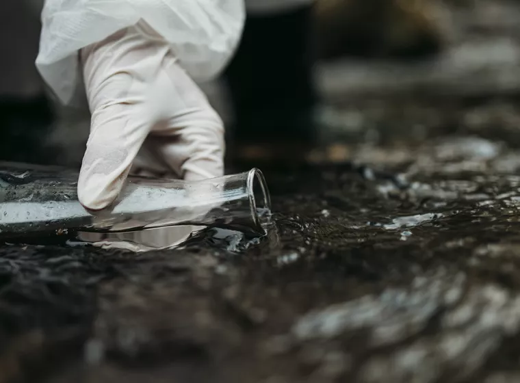 A person sampling fresh water using a test beaker in open environment. Evaluation exposure assessments and toxicity evaluations.