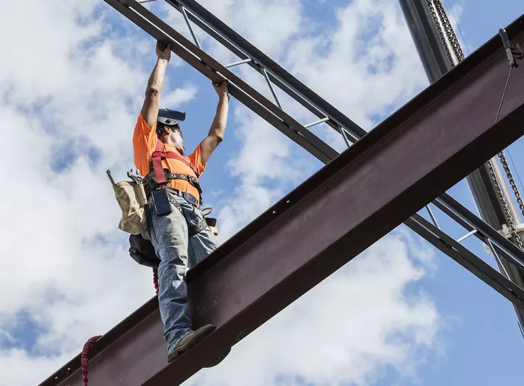 Construction worker stands on an elevated iron I-Beam. Exponent helps reduce cost and maximize ROI through construction cost analysis.