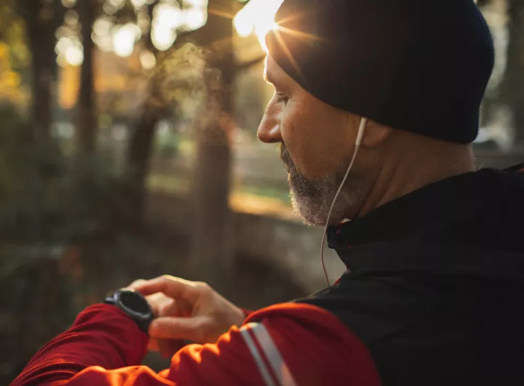 A man on checking his smart watch while on a run through a trail.