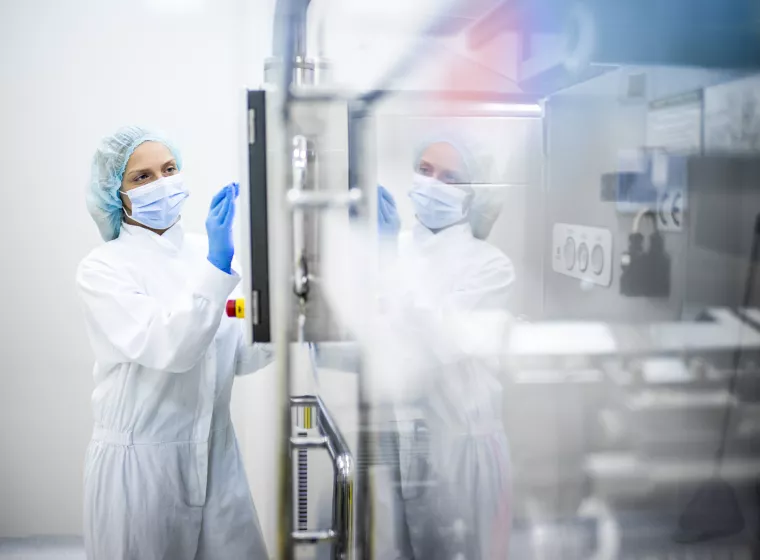 A person wearing proper safety clothes seen taping on the screen of a complex machine in pharmaceutical industry.