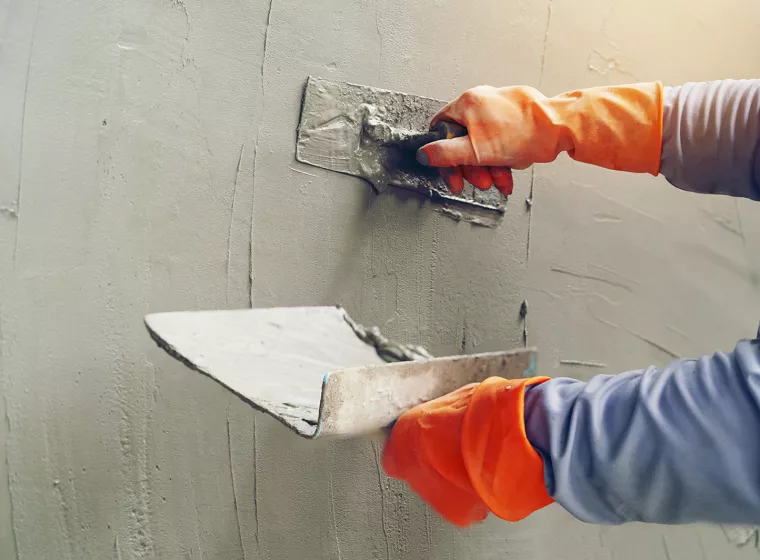 Worker applying stucco application to wall. Exponent conducts testing and analysis of construction products