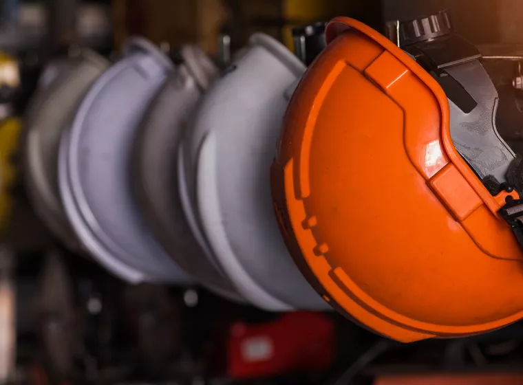 A row of orange industrial hard hats in a row. Exponent provides occupational and industrial workplace safety assessments