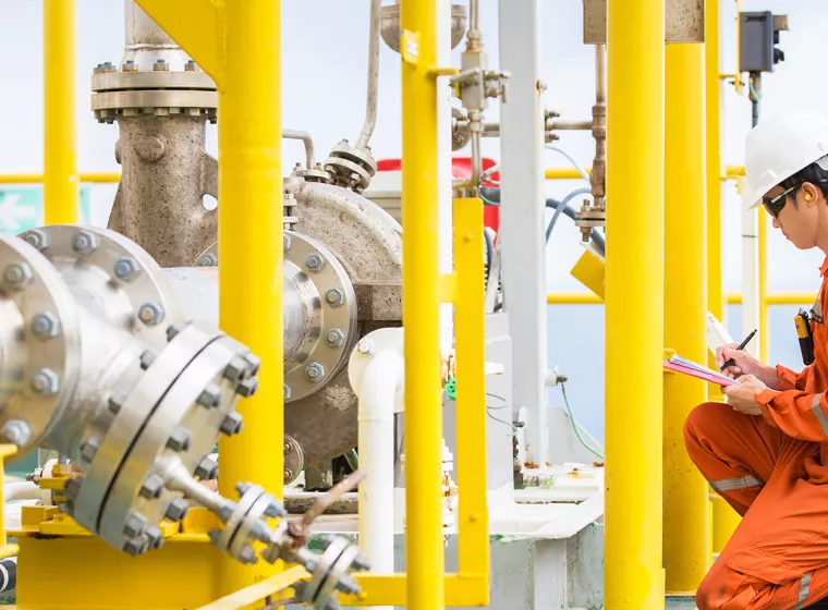 Worker in a factory setting examines a large pipe. Mechanical engineering expertise for all types of corrosion and materials challenges.