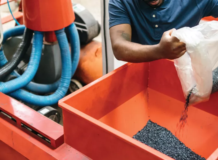 A worker pours a bag of polymer beads into a manufacturing machine. Exponent provides engineering expertise for polymers and plastics.