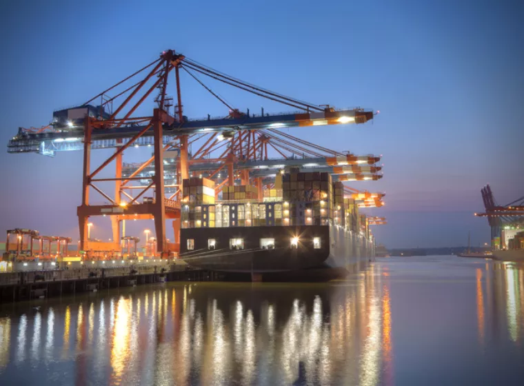Ship docked in the harbor at night with lights reflecting off the water. Exponent provides engineering support for shipping and maritime.