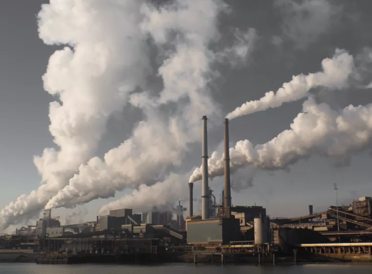 Smoke releases from several stacks at an industrial plant on a waterfront 