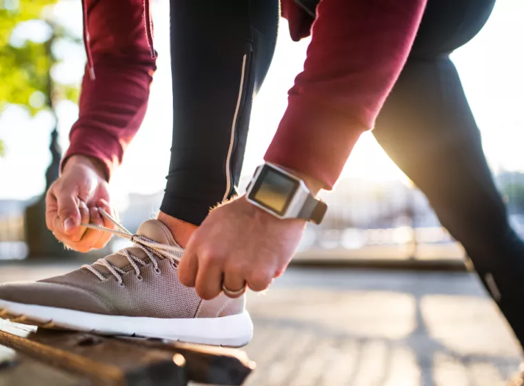 Close up of man in exercise clothing bending down to tie his shoe on a park bench