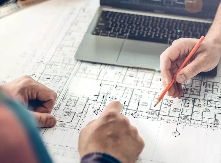 Two people examine construction blueprints while holding pencils. Exponent technical construction consulting. 