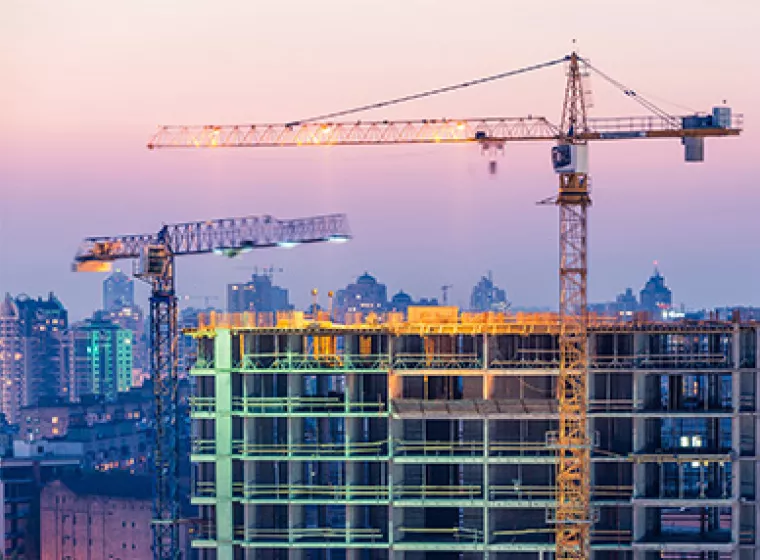 Construction cranes with a city skyline in the background. Exponent construction engineers provide support for all types of projects.