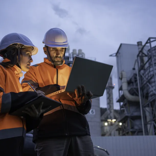 Man and woman working late with laptop in a power plant. Night shift.
