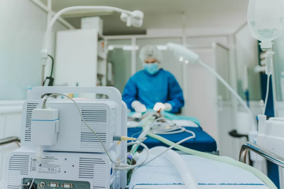 A close up of a patient monitor with a medical professional operating it in the background