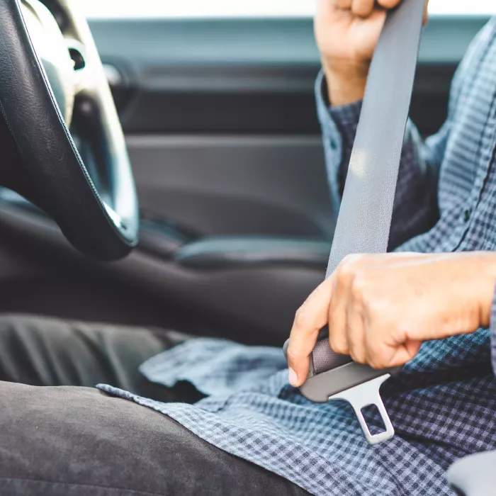 A shot of a person in the behind the steering wheel of a car buckling their seatbelt