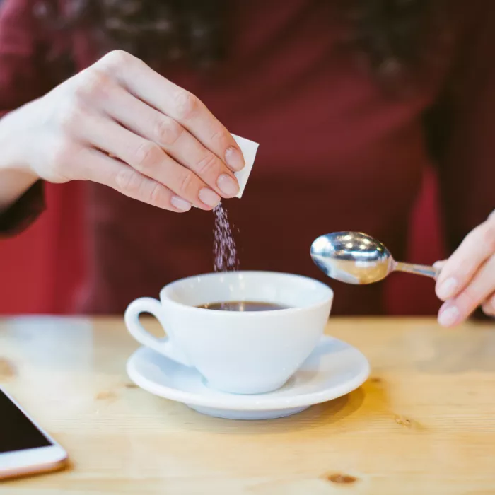 Hands pouring sugar into black coffee