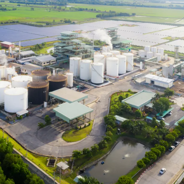 An aerial view of an industrial area with an oil refinery with multiple large storage tanks with a field filled with solar panels in the distance