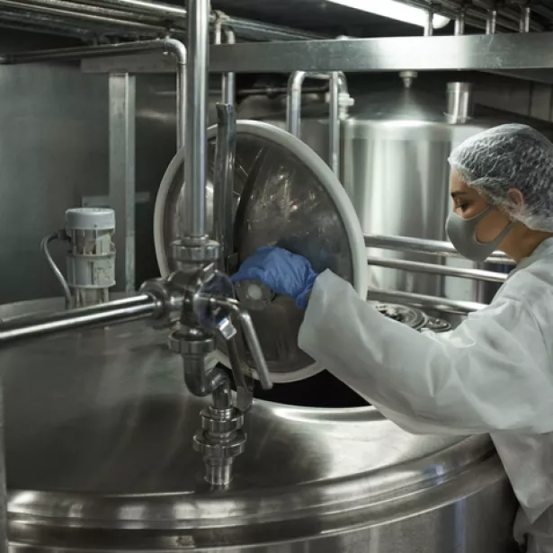 An industrial food factory worker opens a stainless steel vat. Exponent helps food and beverage manufacturers improve food safety.