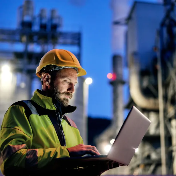 Young engineer wearing a helmet and using a laptop during his night shift. Engineering concept.