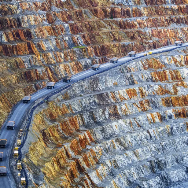 convoy of dump trucks driving through a mining operations area