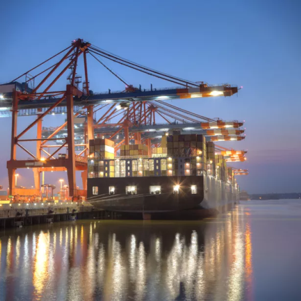 Ship docked in the harbor at night with lights reflecting off the water. Exponent provides engineering support for shipping and maritime.