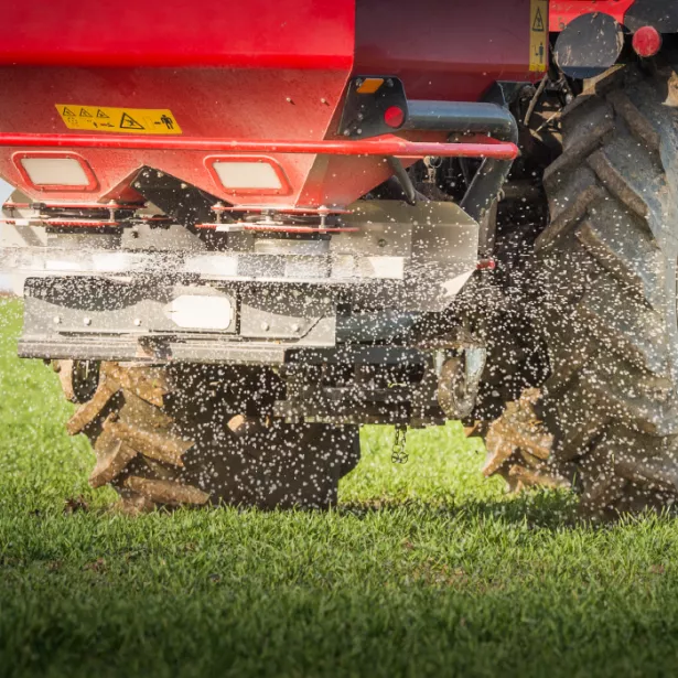 A tractor spreads fertilizer as it drives across a stretch of grass