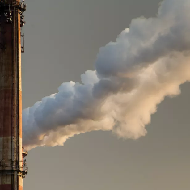 Close up view of two side-by-side smoke stacks releasing thick clouds of smoke into the air