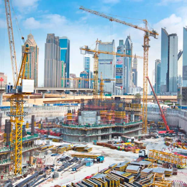 Multiple yellow cranes in large construction pit assembling a building foundation surrounded by high-rise business buildings