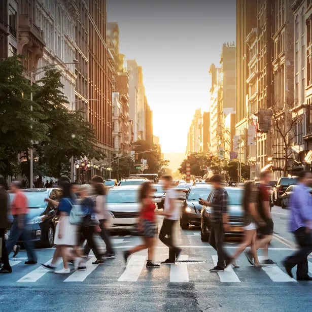 A crowd of people use a cross walk in a large city. Exponent helps build more inclusive technologies for all.