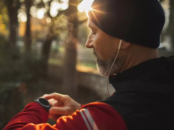 A man on checking his smart watch while on a run through a trail.