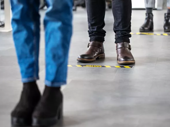 People standing on floor markers to social  distance while waiting in line 