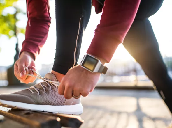 Close up of man in exercise clothing bending down to tie his shoe on a park bench