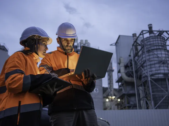Man and woman working late with laptop in a power plant. Night shift.