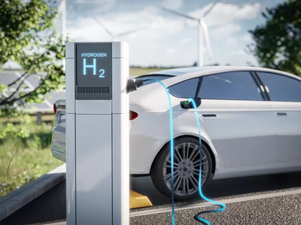 Electric car charging at a hydrogen station, set against a green environment with wind turbines in the background