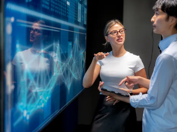 Business meeting in modern office with female programmer explaining infographic on screen to Japanese manager. Teamwork, strategy, innovation, coding, big data, AI, and technology presentation for success.