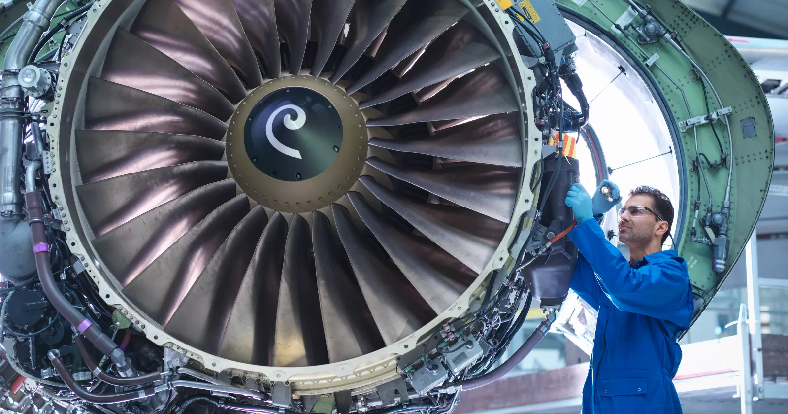 Aviation mechanic standing next to a large jet engine. Exponent provides aeronautical engineering expertise.