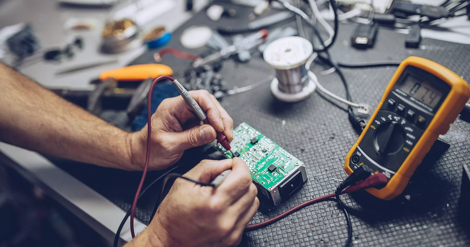 Worker testing electrical computer components using digital multimeter. Exponent conducts technical forensics investigations.