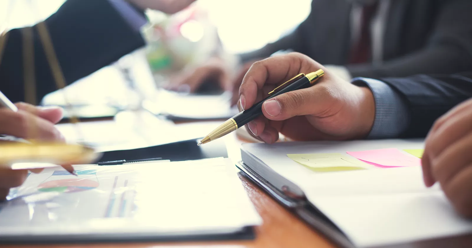 Stakeholders discuss important paperwork at a desk. Exponent provides technical consulting for disputes and claims. 