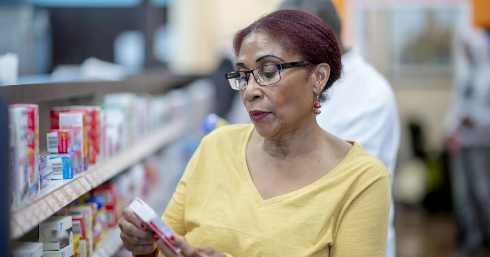 A woman peruses the shelf at a pharmacy, reading the label.