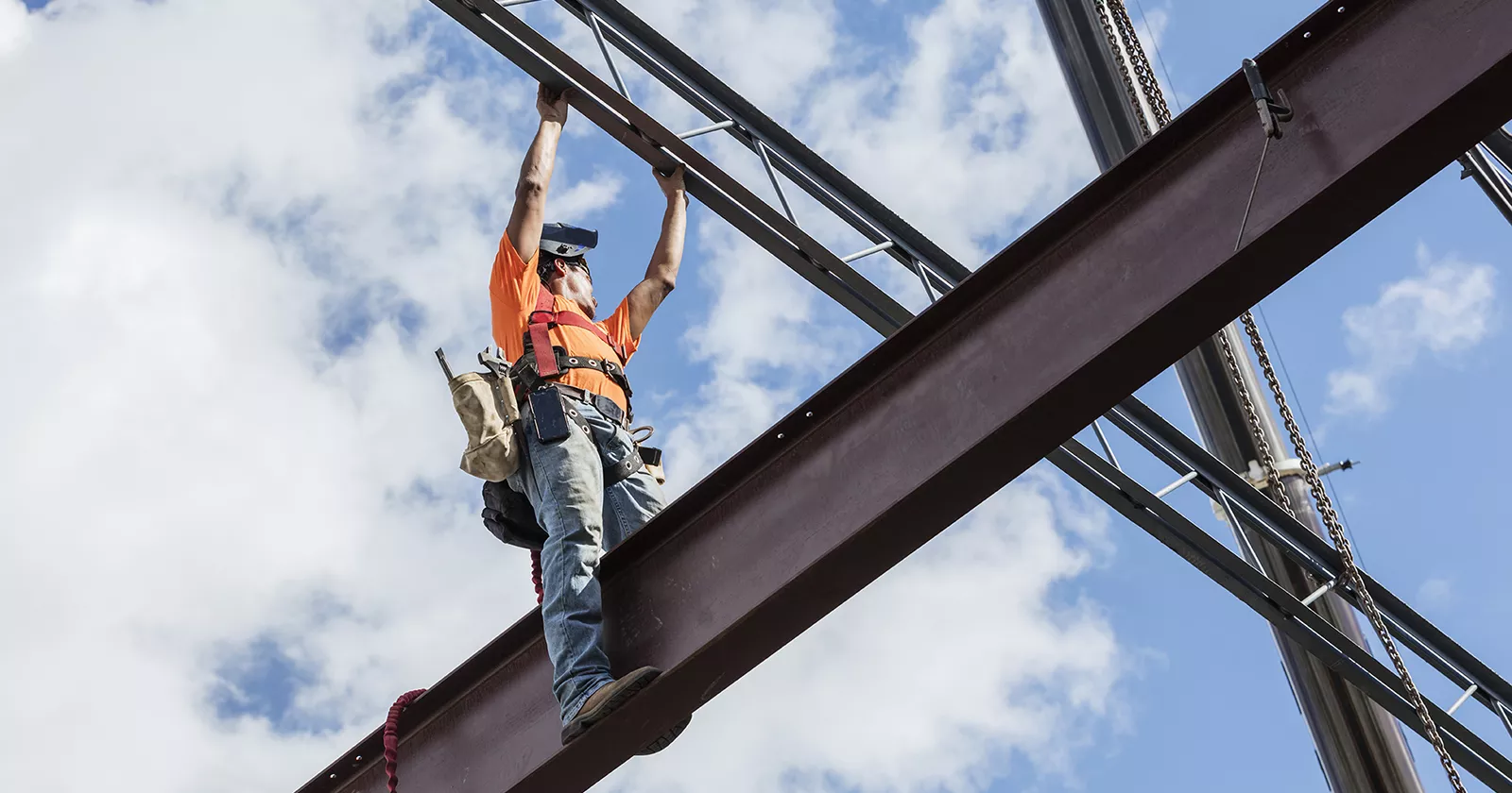 Construction worker stands on an elevated  iron I-Beam. Exponent helps reduce cost and maximize ROI through construction cost analysis.