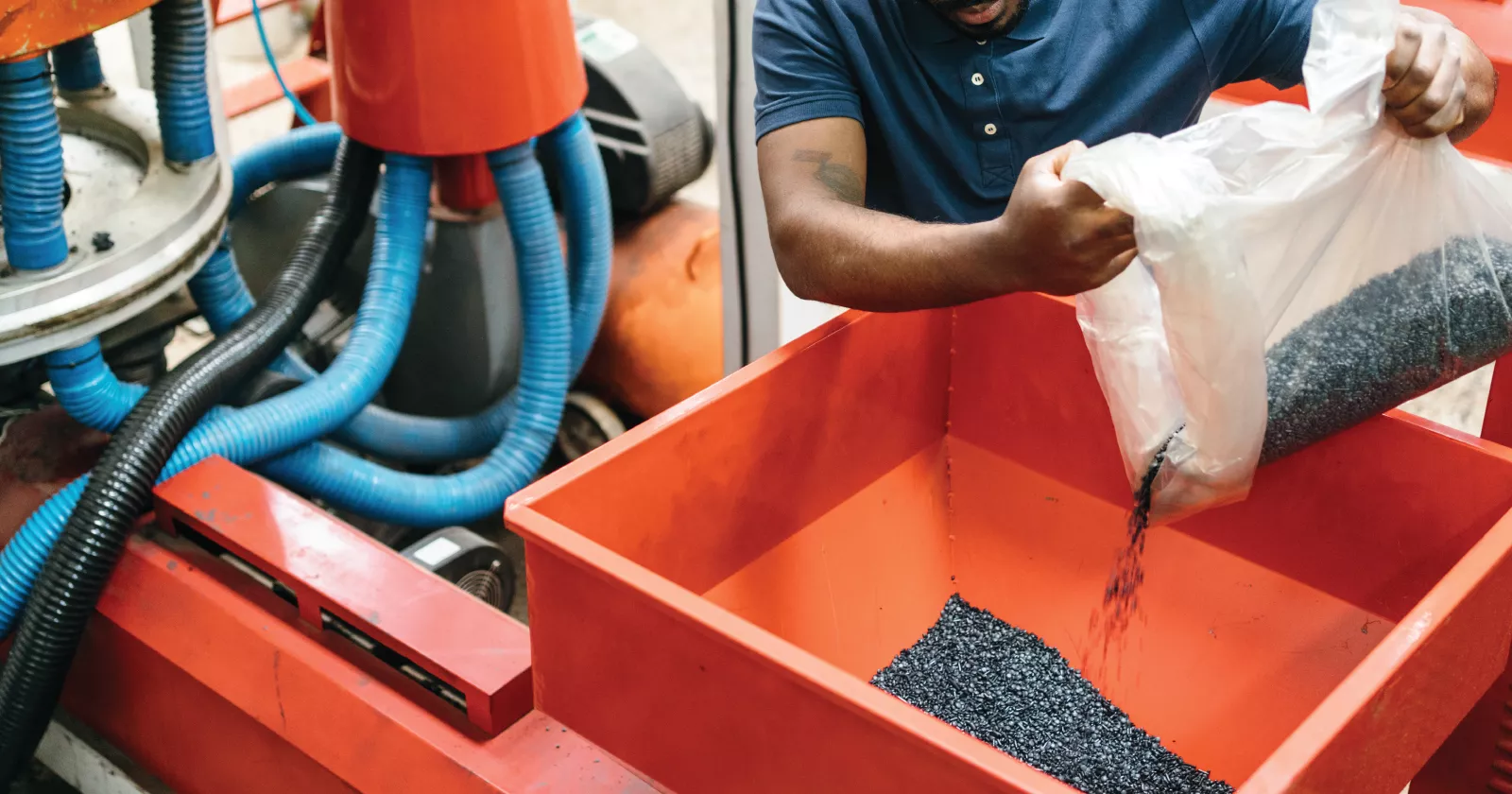 A worker pours a bag of polymer beads into a manufacturing machine. Exponent provides engineering expertise for polymers and plastics.