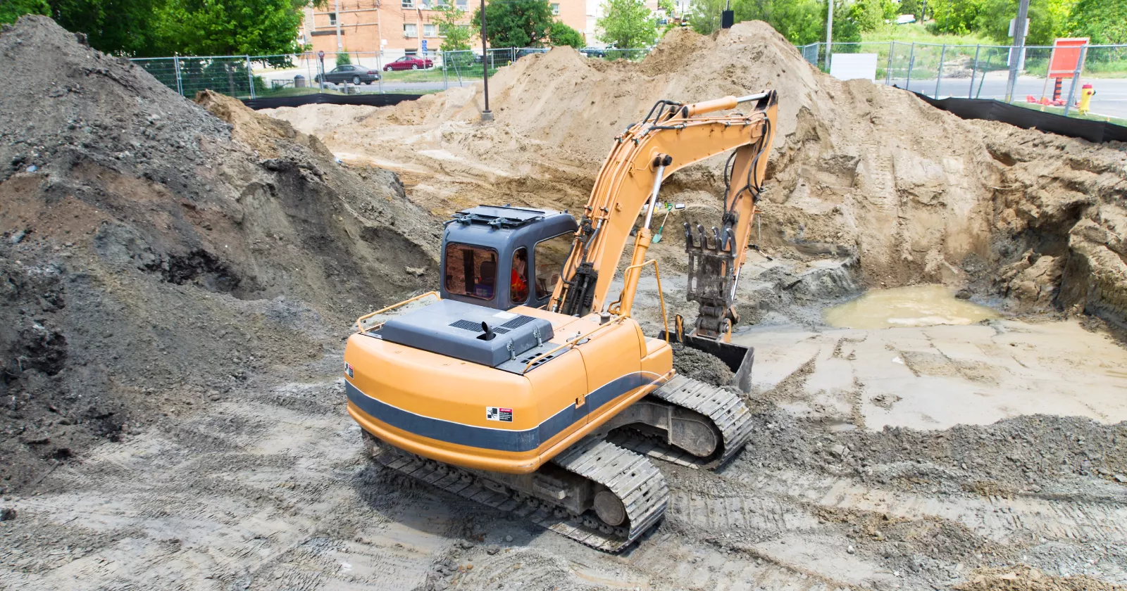 A construction excavator removes contaminated soil from a development site. Exponent helps with environmental site remediation.