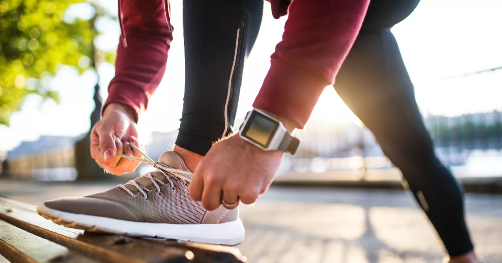 Close up of man in exercise clothing bending down to tie his shoe on a park bench