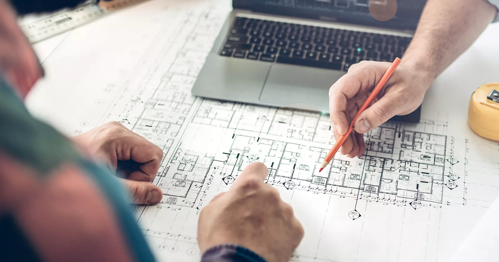 Two people examine construction blueprints while holding pencils. Exponent technical construction consulting. 