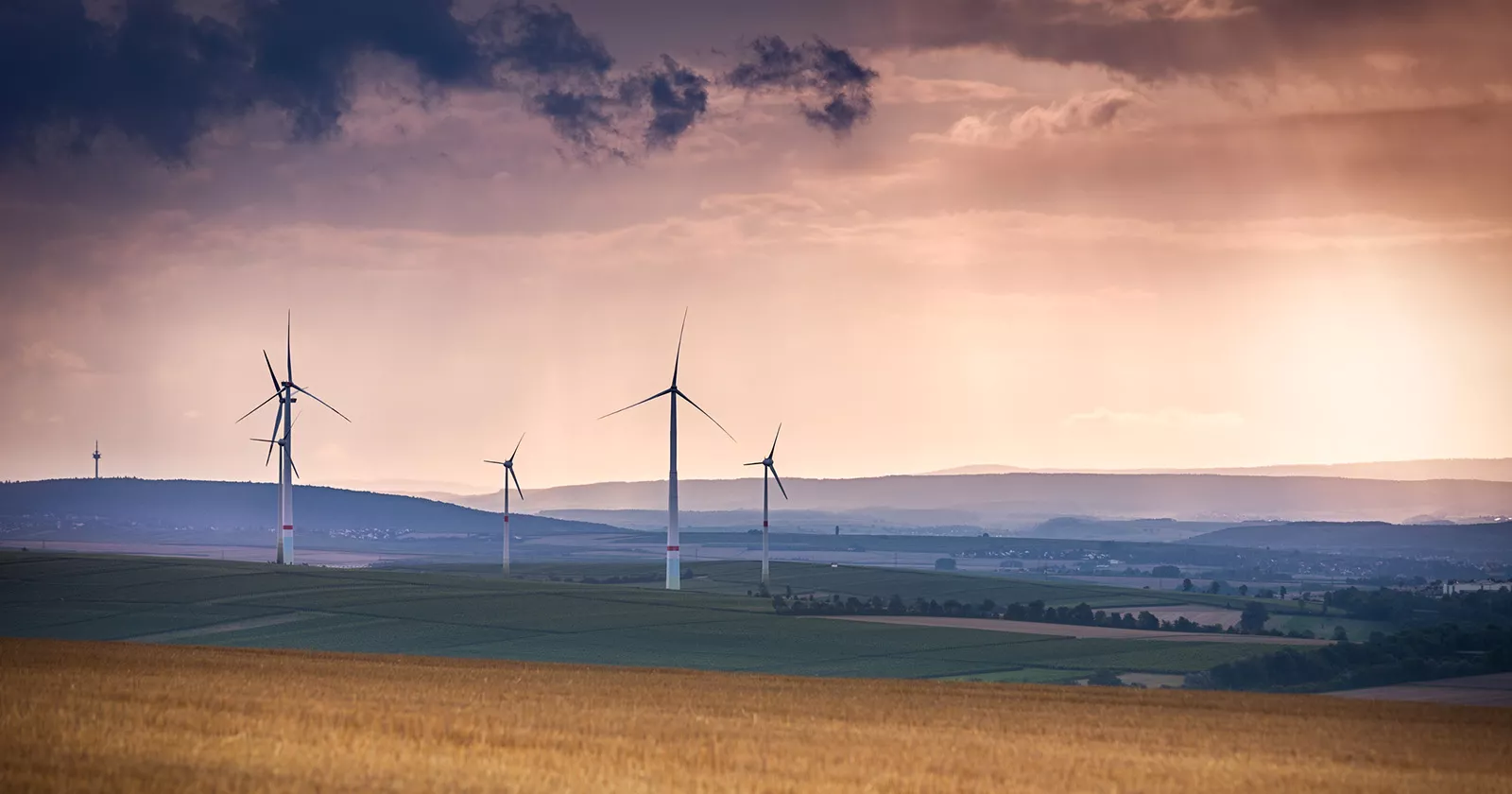 Wind turbines on the horizon are surrounded by clouds. Exponent consultants help clients create a safer more sustainable world.