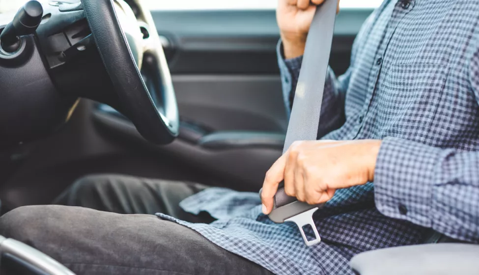 A shot of a person in the behind the steering wheel of a car buckling their seatbelt