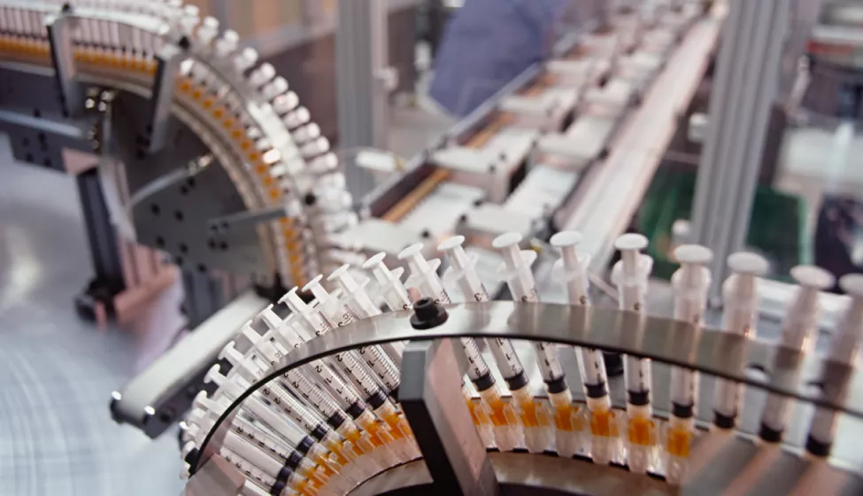 Two conveyor belts with hundreds of syringes merging into a third conveyor belt in a manufacturing plant