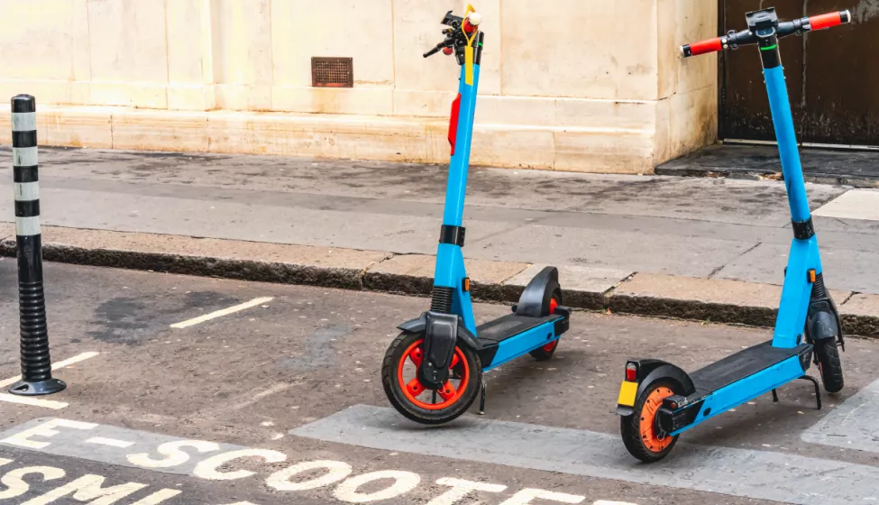 Two blue e-scooters parked at the curb