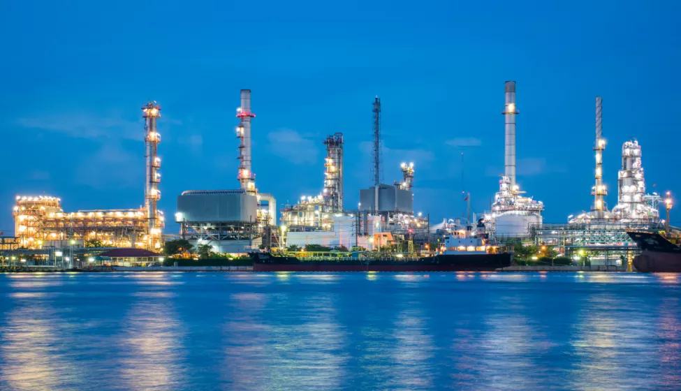 Brightly lit industrial facilities at night along the shoreline of a bay